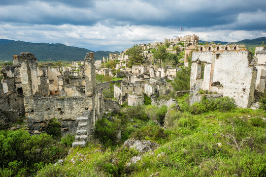 Abandoned stone houses of Kayak&ouml;y ghost town village surrounded by green spring nature under a stormy sky, Fethiye, Turkey