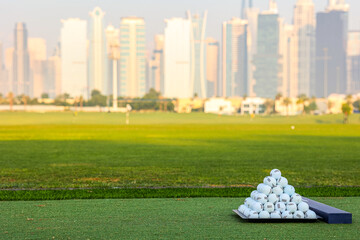 A pyramid stack of golf balls on a green turf with a modern city skyline in the background, blending sports and urban living. Pyramid of Golf Balls with City Skyline