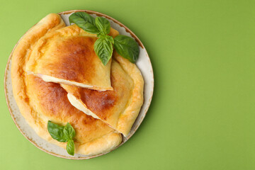 Pieces of delicious calzone pizza with mozzarella, tomatoes and basil on green background, top view. Space for text