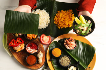 Woman holding piece of banana leaf and bowl with tasty food at white table, top view. Healthy eco...