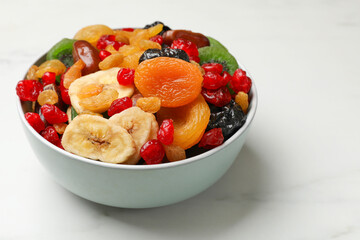 Mix of different dried fruits in bowl on white marble table, closeup