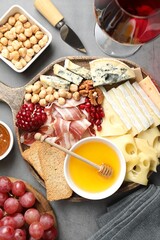 Different types of cut cheese and other snacks served with wine on gray textured table, flat lay