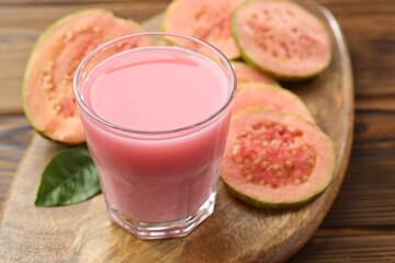 Tasty guava juice in glass, leaf and slices of fruits on wooden table, closeup