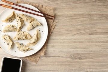 Delicious gyoza dumplings with sesame seeds served on wooden table, top view. Space for text