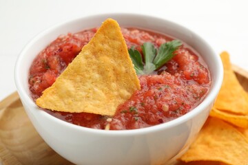 Delicious spicy salsa sauce with nacho chip in bowl on white table, closeup