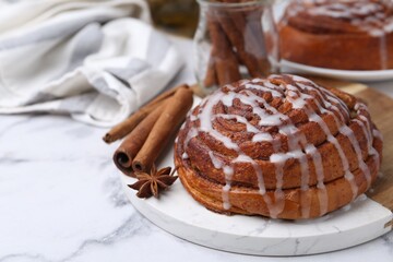 Tasty cinnamon roll with cream and spices on white marble table, closeup