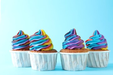 Delicious cupcakes with colorful cream on light blue background, closeup