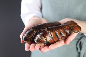 Woman with raw lobster tails on dark grey background, closeup