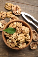 Peeled walnuts in bowl and nutcracker on wooden table, flat lay