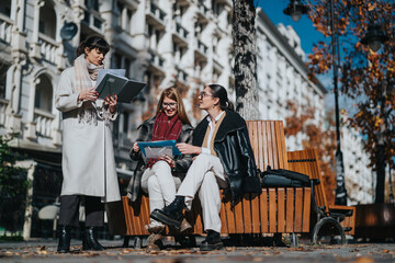 Three businesswomen interact in an outdoor urban setting, surrounded by autumn foliage.