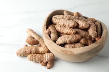 Raw turmeric roots in bowl on white marble table, closeup