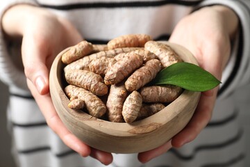 Woman holding bowl with raw turmeric roots, closeup