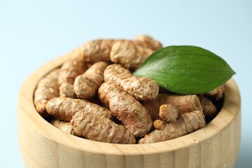 Tumeric rhizomes with leaf in bowl on light blue background, closeup