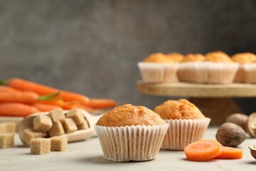 Tasty carrot muffins, fresh vegetables, sugar and walnuts on light grey table, closeup