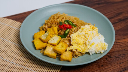 A plate of fried noodles served with egg and fried tofu. Topped with red and green chilies.