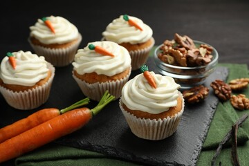 Tasty carrot muffins with cream, walnuts and fresh vegetables on black wooden table, closeup