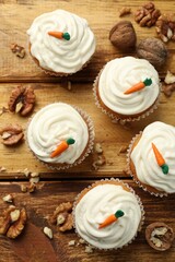 Delicious carrot cupcakes and walnuts on wooden table, flat lay
