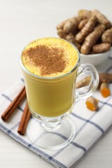 Delicious turmeric latte and rhizomes on white wooden table, closeup