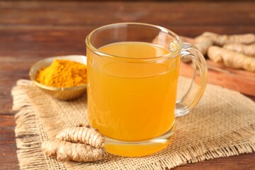 Aromatic turmeric tea in glass mug, roots and powder on wooden table, closeup