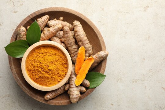 Aromatic turmeric powder in bowl, fresh roots and leaves on light grey table, top view. Space for text