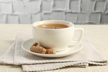 Aromatic turmeric tea and rhizomes on white textured table, closeup