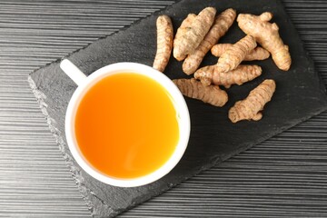 Aromatic turmeric tea and rhizomes on black table, top view