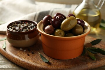 Tasty olives in bowl, leaves and spices on wooden table, closeup