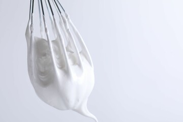 Whisk with whipped cream on white background, closeup. Space for text