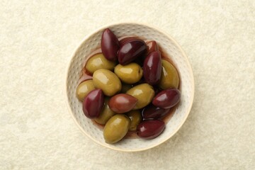 Tasty marinated olives in bowl on beige table, top view