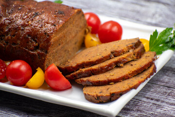 Vegan meat alternative- seitan seasoned with spiced, glazed with BBQ sauce. White plate, sliced, wooden table.