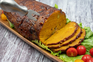Vegan meat- seitan- ham shaped and served on wooden tray, salad greens. Wooden table, copy space