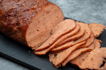 Vegan meat alternative- seitan  made with gluten and tofu, seasoned with spices, glazed with BBQ sauce. White plate, sliced, slate board