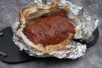 Vegan meat alternative- seitan  made with gluten and tofu, seasoned with spices, glazed with BBQ sauce. White plate, sliced, slate board
