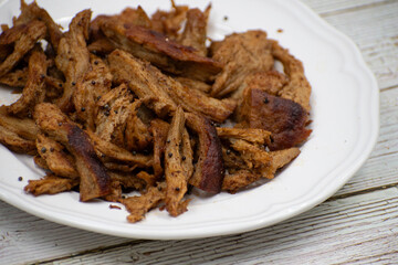 Shredded seitan, mock chicken, on white plate, wooden table. Copy space.