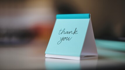 A turquoise thank you note rests on a surface