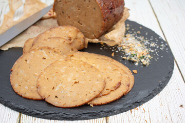 Seitan shaped and cooked in ham press, sliced on slate board. Vegan protein, plant based alternative to meat.