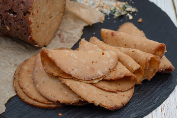 Seitan shaped and cooked in ham press, sliced on slate board. Vegan protein, plant based alternative to meat.