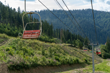 Fototapeta premium Ski lift in green forest. Cableway in Mountains. Summer nature outdoor trees