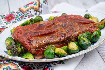 Vegan pork bellly roast made with seitan and starch, served on oval plate along with roasted Brussels sprouts. Wooden table, stylish setting