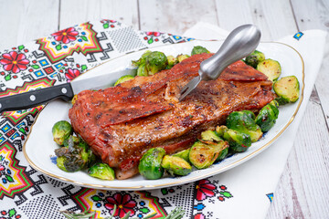 Vegan pork bellly roast made with seitan and starch, served on oval plate along with roasted Brussels sprouts. Wooden table, stylish setting