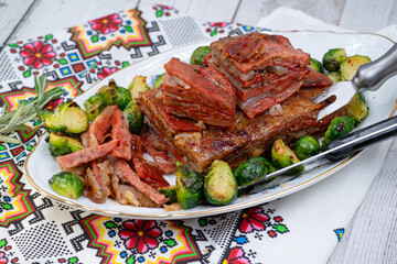 Vegan pork bellly roast made with seitan and starch, served on oval plate along with roasted Brussels sprouts. Wooden table, stylish setting