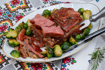 Vegan pork bellly roast made with seitan and starch, served on oval plate along with roasted Brussels sprouts. Wooden table, stylish setting