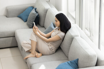Obraz premium Top view young attractive Asian woman spend time in modern spacious living room with smartphone, taking selfie pictures, record video for social media. Pastime on internet, mobile application usage