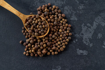 allspice or Jamaican pepper in a wooden spoon on a black stone table, top view.