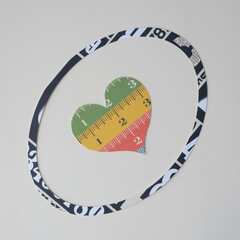 decorative paper heart with measuring tape pattern inside an oval paper ring on a blank surface