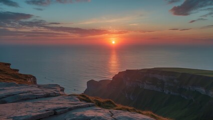 Sunset over ocean cliffs with dramatic sky colors and reflections on water near coastal landscape with grassy edges and rocky foreground