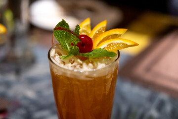 Close up view of orange cocktail, with cherry and sliced orange on top. On the table with bokeh background