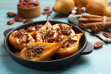 Delicious pears with caramel sauce, pecan nuts and thyme on light blue wooden table, closeup
