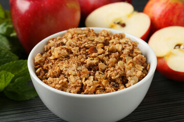 Delicious apple crisp in bowl, fresh fruits and mint on black textured table, closeup