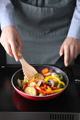 Woman frying vegetables and mushrooms in pan on stove, closeup